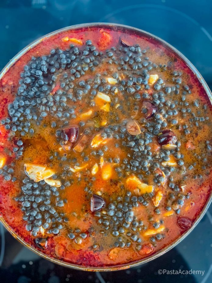 Sardijnse fregola met tomaat en vis in een grote kookpot